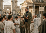 Guide addressing group at Roman Forum beneath sign reading FORVM ROMANVM
